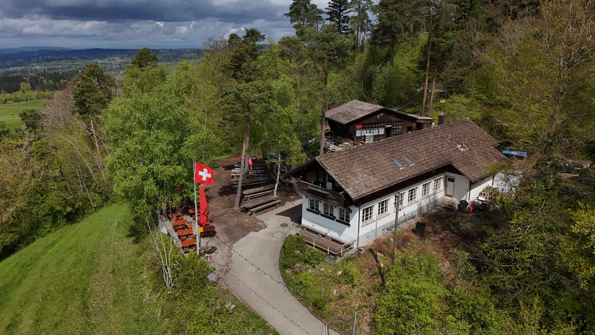 Nach sechs Wochen wieder geöffnet: das beliebte Berggasthaus Rosinli in Adetswil. Luftaufnahme eines Restaurants auf einem Berg mit Schweizer Fahne.